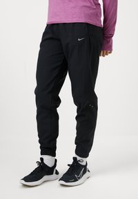 Czarne spodnie sportowe z lekko teksturowanej powierzchni, z elastycznym paskiem w talii i mankietami. Logo Nike w kolorze srebrnym na lewym udzie.