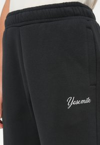 Czarne dresy wykonane z miękkiego materiału, z elastycznym pasem, z białym, haftowanym logo "Yosemite" z boku.