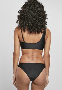 Fekete bikini szett, letisztult, minimalista designnal. A melltartó állítható pántokkal rendelkezik, az alsó rész alacsony derekú vágású és sima textúrájú.