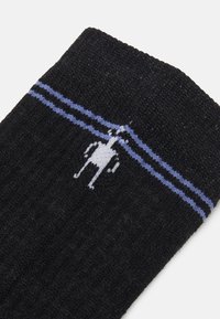 Svart ribbestrikkede sokker med en hvit tegneseriefigur og to horisontale blå striper nær toppen. Myk tekstur og standard crew lengde.