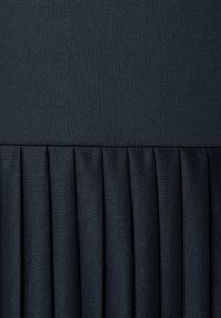 Granatowy materiał z plisami, z gładką górną częścią, z drobno przeszytymi plisami na dole, tworzącymi teksturowany, warstwowy wygląd.