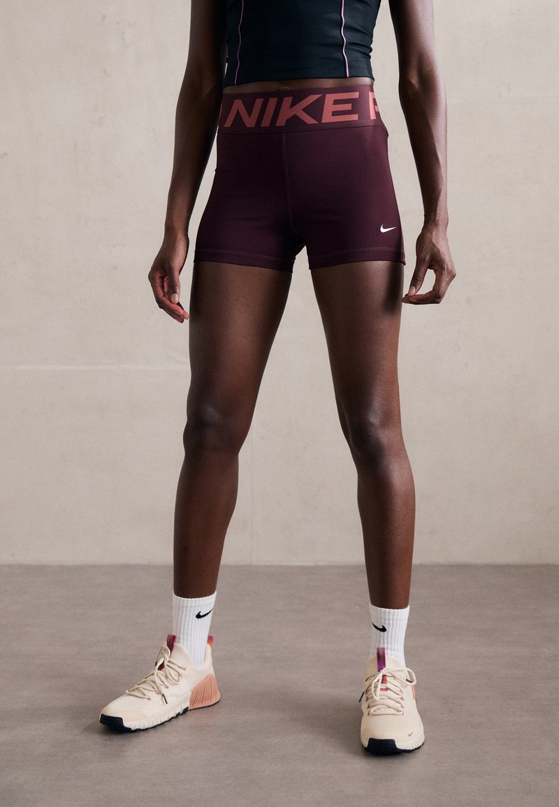 Nike maroon athletic shorts with wide contrasting logo waistband, paired with beige sneakers and white crew socks with black logo.