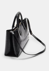 Sac fourre-tout en cuir noir plissé avec deux poignées et une bandoulière amovible, présentant un intérieur spacieux et une fermeture éclair dorée.