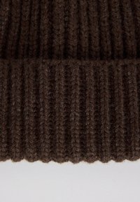 Cappello lavorato a maglia marrone con texture a coste, realizzato in una morbida miscela di lana. L'orlo è leggermente arrotolato per un look casual.