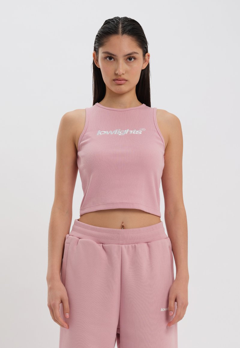 Top scurt roz cu nervuri și logo alb, având un guler înalt și un design fără mâneci. Stilizat cu pantaloni sport roz asortați.