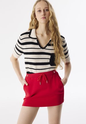Gestreepte gebreide polo in roomwit en zwart, gecombineerd met een rode rok met een trekkoord en zijzakken, met metallic accenten.