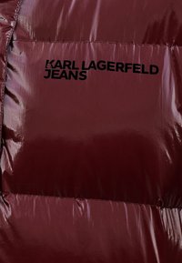 Burgundy quilted puffer jacket with shiny finish; features "KARL LAGERFELD JEANS" logo in black. Textured surface, visible stitching.