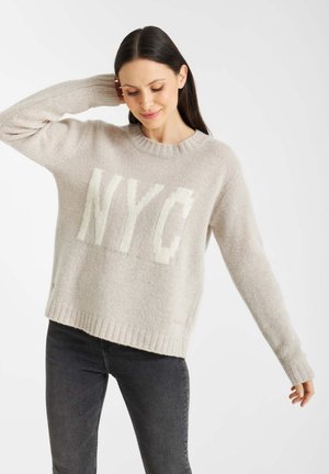 Lichtbeige gebreide trui met een groot wit "NYC"-grafiek. Geribde ronde halslijn en manchetten, met een relaxte pasvorm en zachte textuur.