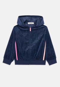 Felpa con zip in velluto blu navy con texture scintillante, strisce laterali rosa e polsini elasticizzati. Include un cappuccio e una chiusura con zip frontale.