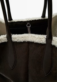 Bruine leren draagtas met zachte crèmekleurige schapenvachtbies, voorzien van een zwart interieur, dubbele handvatten en een metalen ritssluiting.