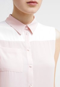 Light pink sleeveless blouse with a button-up front, pointed collar, and small chest pocket. Smooth fabric with a slightly sheer texture.