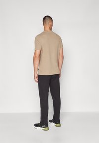 Tajt beige kortärmad t-shirt med ett texturerat mönster, kombinerad med svarta byxor och svarta sneakers med gröna accenter.