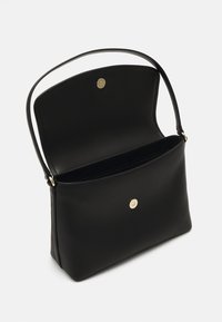 Borsa a mano in pelle nera con una superficie texturizzata, una forma strutturata, manico superiore e chiusura a pulsante dorato. L'interno non è foderato.