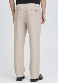 Béžové kalhoty s přímým střihem, vyrobené z hladké tkaniny, se dvěma zadními kapsami a elastickým pasem.