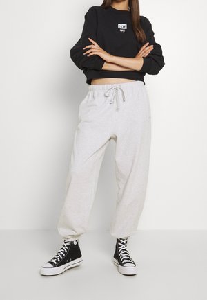 Sudadera negra cortada con un logo blanco, combinada con pantalones de chándal gris claro que cuentan con una cintura elástica con cordón y zapatillas altas negras.