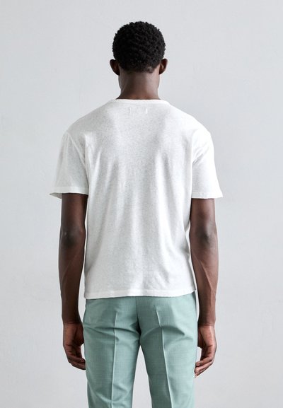 Weißes Baumwoll-T-Shirt mit kurzen Ärmeln, Rundhalskragen und lässiger Passform, kombiniert mit hellgrünen, maßgeschneiderten Hosen.