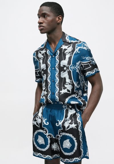 Košile s krátkým rukávem a odpovídající kraťasy z hladké látky, zdobené modrým, černým a bílým složitým zvířecím vzorem a knoflíky.