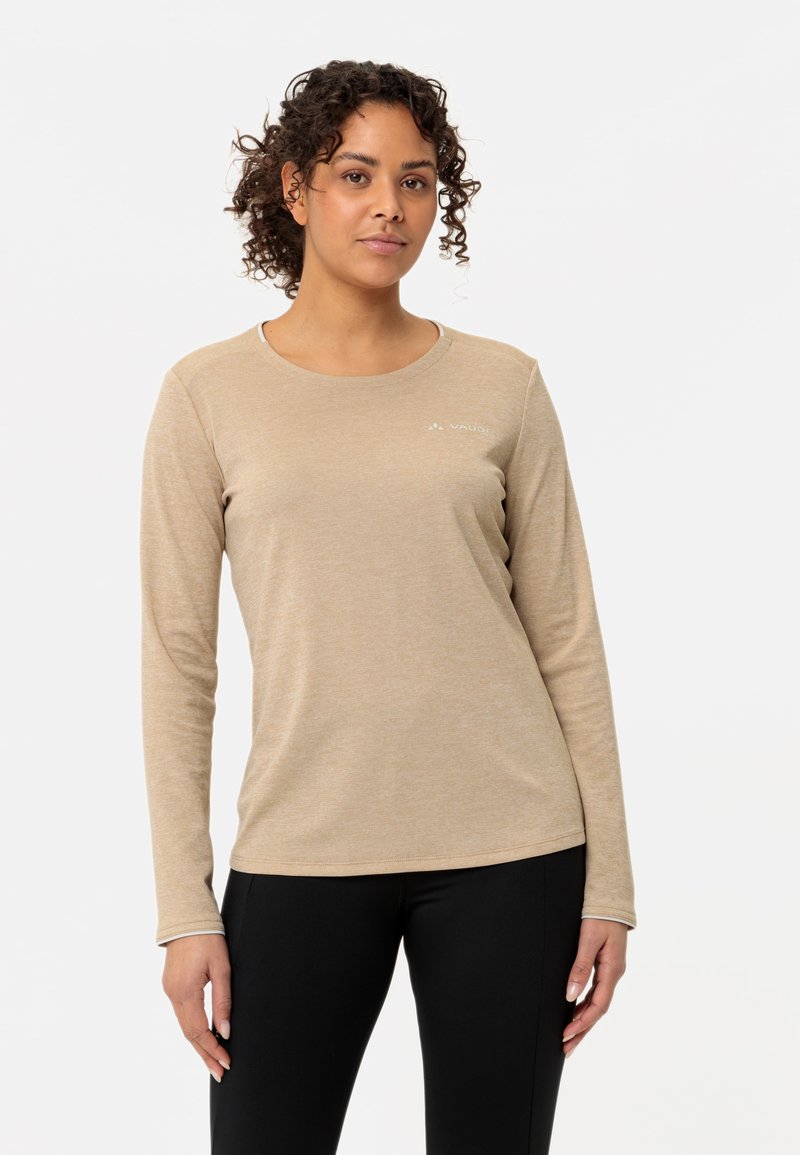 Langermet beige skjorte med rund hals og subtil tekstur, med en liten hvit logo på øvre venstre side, kombinert med svarte leggings.