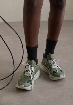Zapatillas de malla verdes con acentos grises y cordones blancos, combinadas con calcetines negros con canalé. Presentan una suela gruesa y un diseño aerodinámico.