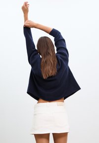 Marineblauer Strickpullover mit weiten Ärmeln, kombiniert mit einem weißen Denim-Minirock. Mit abgerundetem Saum und sichtbarem Bund.