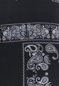 Tela negra con intrincados patrones de paisley blancos. El diseño incluye secciones bordeadas con diversos motivos de paisley y acentos florales.