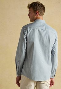 Jasnoniebieska koszula w białe paski z kołnierzykiem zapinanym na guziki i długimi rękawami, wykonana z gładkiego materiału, z karczkiem z ty�łu i mankietami zapinanymi na guziki.