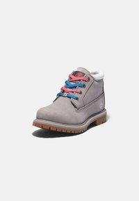 Bota de cuero gris hasta el tobillo con cordones rosa y azul, cuello blanco y suela marrón rugosa, con un logo en el lateral.