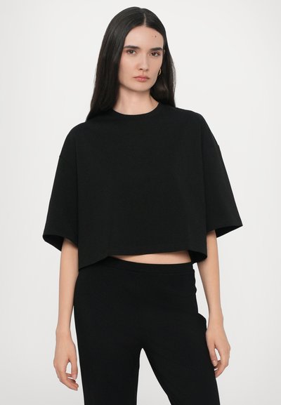 Schwarzes, kurzärmeliges Crop-Top aus einem weichen, glatten Stoff mit einem runden Ausschnitt und weiten Armöffnungen, kombiniert mit passenden schwarzen Hosen.