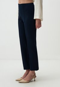 Pantalons ajustés bleu marine en tissu lisse, avec des coutures latérales et une coupe droite, associés à des escarpins beiges à talons slingback.
