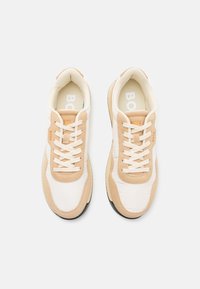White and beige sneakers with textile and suede material, featuring round toes, lace-up design, textured soles, and embossed logo.