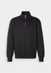 Sweat-shirt noir à fermeture éclair quart, col haut, manches longues, poignets et ourlet côtelés, avec petit logo rouge, blanc et bleu sur la poitrine.
