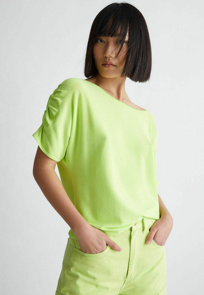 Top lime verde, a maniche corte con design off-shoulder. Tessuto morbido con dettagli arricciati sulle maniche. Abbinato a pantaloni abbinati di un verde chiaro.