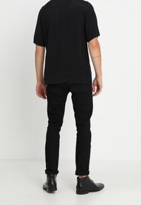 Zwarte shirt met korte mouwen, zwarte slim-fit broek en zwarte enkellaarsjes. Eenvoudig ontwerp met een gladde textuur. Gericht op een donker kleurenpalet.