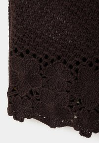 Tissu crocheté brun foncé avec motifs floraux et bord festonné.