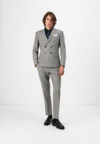 Grå dubbelknäppt kostym med randigt mönster, har slim-fit byxor, en vit fickduk och svarta loafers mot en neutral bakgrund.