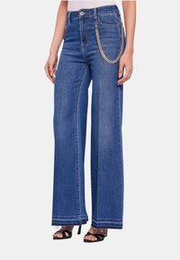 Jeans a gamba larga in denim blu. Caratterizzati da una vita alta, dettagli in catena sui lati e orlo sfrangiato in fondo.
