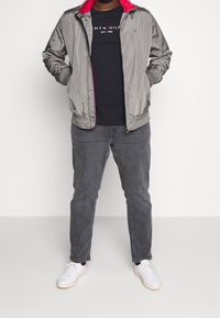 Gray lightweight jacket with red accents, black t-shirt, gray jeans, and white sneakers. The jacket features a zip closure and side pockets.