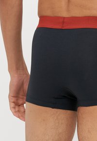 Fekete boxeralsó piros elasztikus derékpánttal, sima textúrával és testhez álló fazonnal, közepes hosszúságú kivágással, látható minták nélkül.