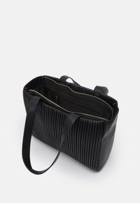 Svart läder tote-väska med vertikala veck, toppdragkedjestängning och två handtag. Inuti finns fickor för organisation.