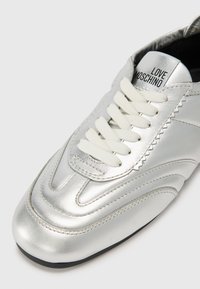 Sneakers de couro prateado com atacadores brancos e um design texturizado. Apresentam uma ponta arredondada e a marca "LOVE MOSCHINO" na língua.