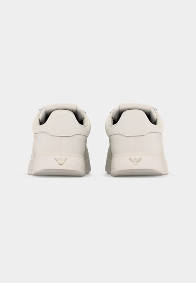 Ζευγάρι λευκά αθλητικά παπούτσια χαμηλού προφίλ, εμφανιζόμενα από πίσω, με μικρό ανάγλυφο λογότυπο στη φτέρνα κάθε παπουτσιού.