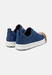 Zapatillas de ante azul con suelas blancas, que cuentan con una caperuza de goma marrón única en la punta. Se muestran dos pares desde el ángulo trasero.