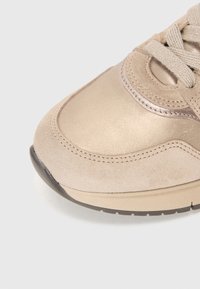 Baskets beiges vues de face avec cuir suédé et cuir métallique, lacets beiges et semelle en caoutchouc beige et noire sur fond clair.