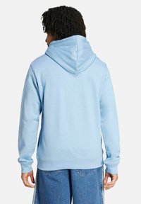 Felpa con cappuccio azzurro chiaro, dal taglio morbido e rilassato, con una texture soffice e polsini a costine. Presenta un cappuccio spazioso e una tasca a marsupio.