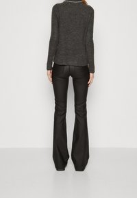 Pantaloni neri a zampa con finitura lucida, abbinati a un maglione a coste grigio scuro con scollo tondo e maniche testurizzate.