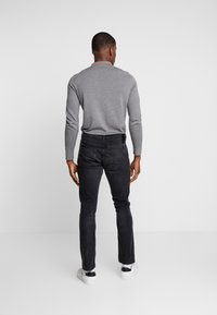 Gray long-sleeve shirt paired with black slim-fit jeans, visible back pockets, and white sneakers against a plain white background.