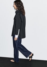 Black pinstriped oversized shirt with white cuffs, paired with loose dark denim jeans and strappy black high-heeled sandals.