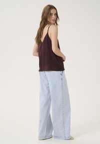 Top in satin bordeaux con spalline sottili, abbinato a jeans a gamba larga blu chiaro. Tessuto morbido con una vestibilità rilassata.