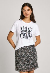 Bílá bavlněná trička s květinovým grafickým designem "Pepe Jeans"; kombinováno s černou sukní s barevným paisley vzorem a elastickým pasem.