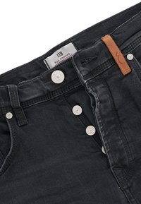 Jeans de mezclilla negra con cremallera y cierre de botón, con un parche de cuero marrón en la cinturilla y botones metálicos blancos.